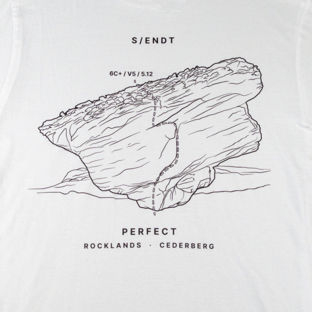 White t-shirt featuring a black line art graphic of a rock formation with a boulder on it, and text reading 'S/ENDT', 'PERFECT', and 'ROCKLANDS • CEDERBERG'.