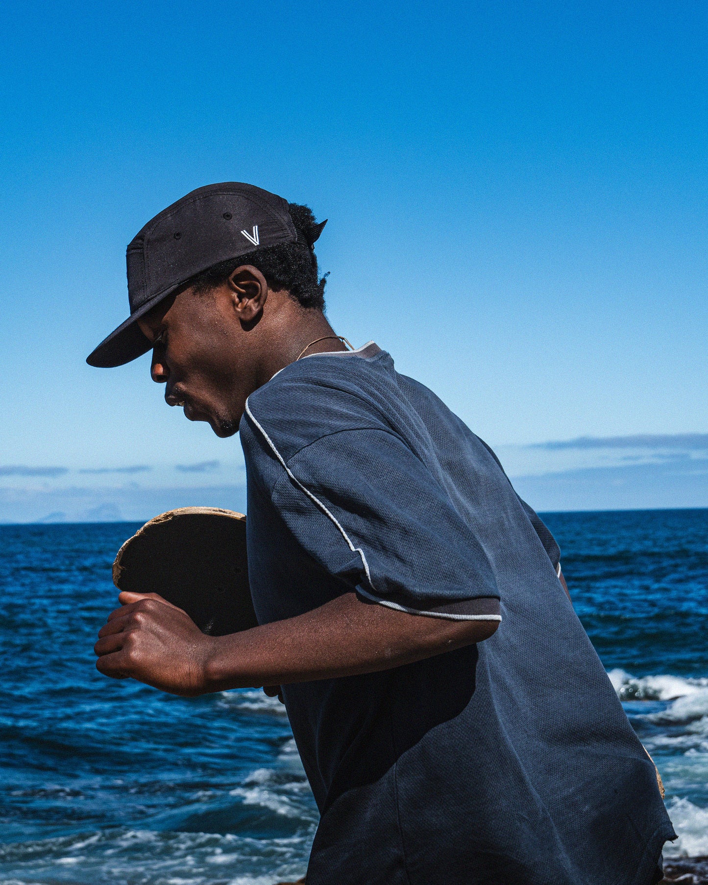 Person holding a skateboard by the ocean with a clear blue sky
