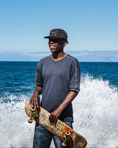 Man holding a skateboard by the ocean with waves crashing in the background