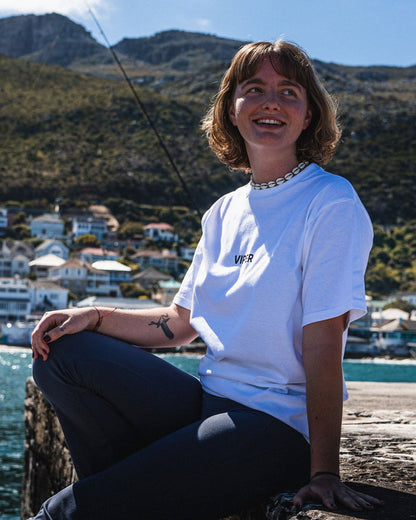 Woman sitting by a waterfront with mountains and buildings in the background