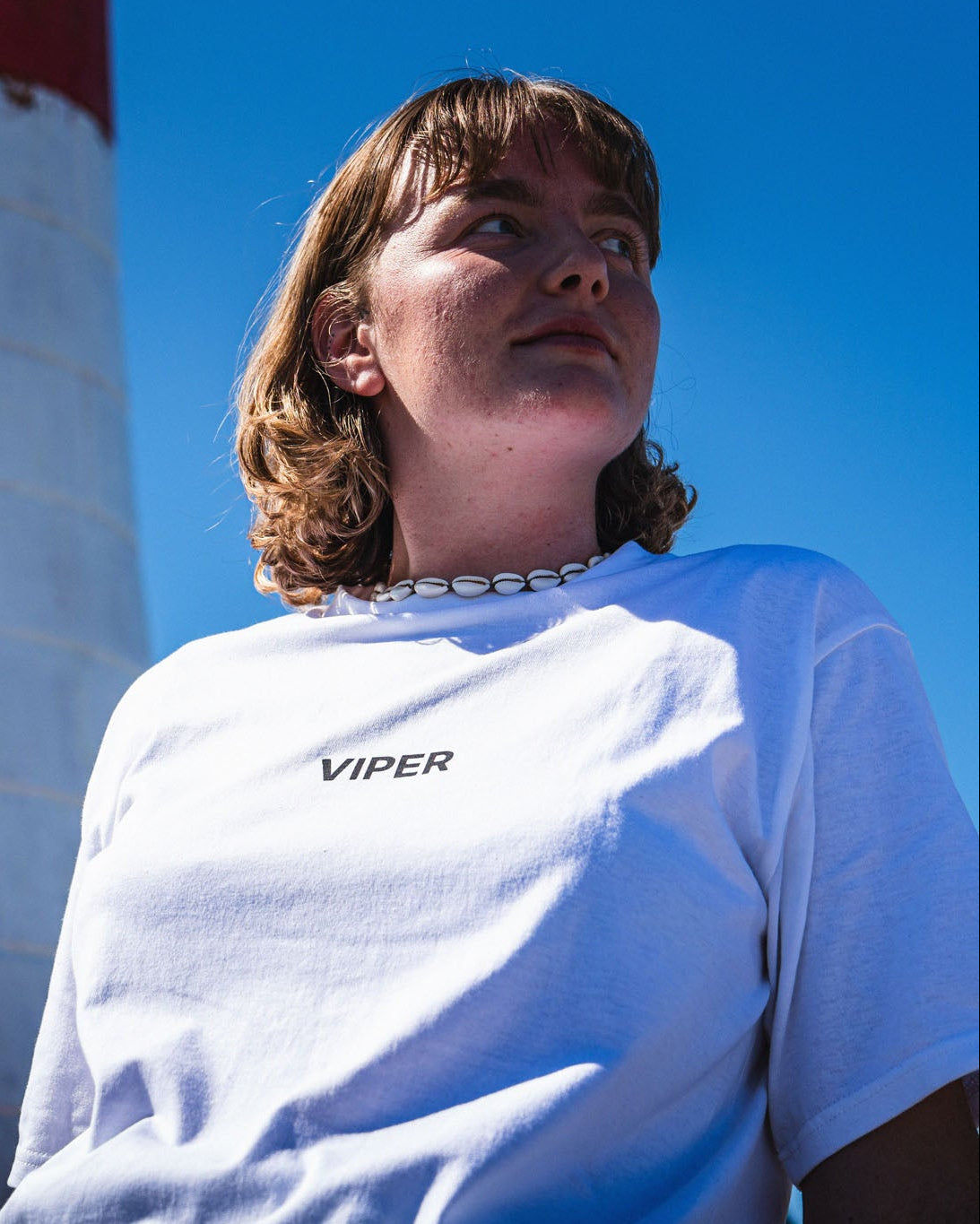 woman wearing a white 'Viper' t-shirt with a lighthouse in the background