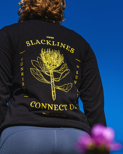 Woman wearing a black sweatshirt with yellow text and design, sitting against a blue background with flowers.