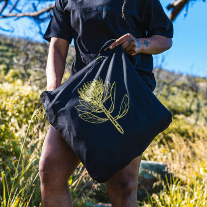 Person holding a black tote bag with a plant design outdoors