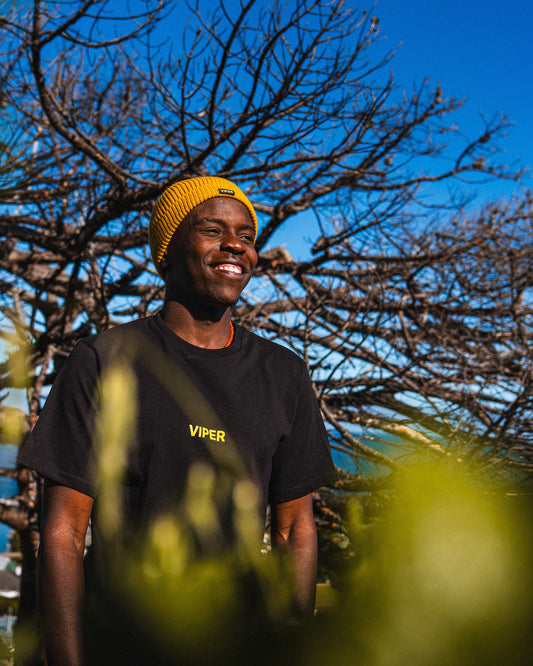 Person wearing a black 'Viper' t-shirt and yellow beanie standing outdoors with trees and blue sky in the background.