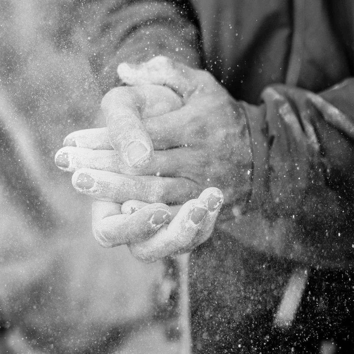 Black and white close-up of a person's hands covered in climbing chalk with fine particles suspended in the air.